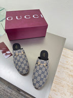 Women’s Gucci GG-pattern slide mules, angled view with black insoles and gold-tone hardware