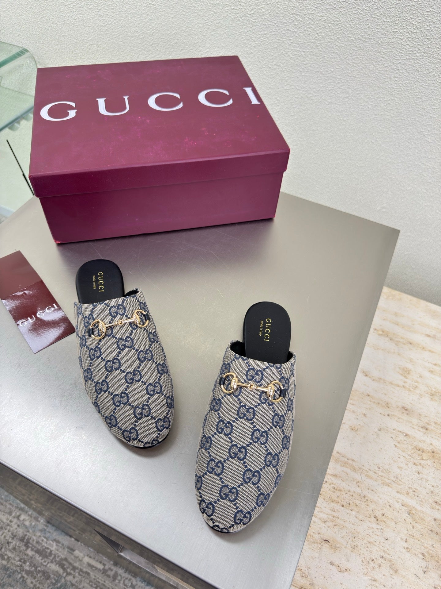 Women’s Gucci GG-pattern slide mules, angled view with black insoles and gold-tone hardware