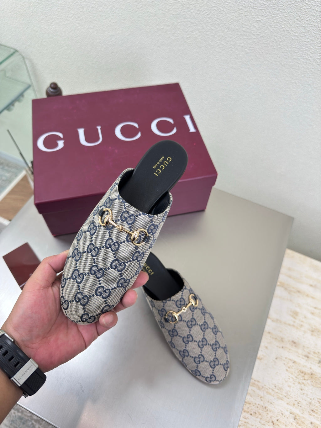 Women’s Gucci GG-pattern slide mules held in hand, showing gold-tone horsebit detail