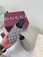 Women’s Gucci GG-pattern slide mules held in hand, showing gold-tone horsebit detail