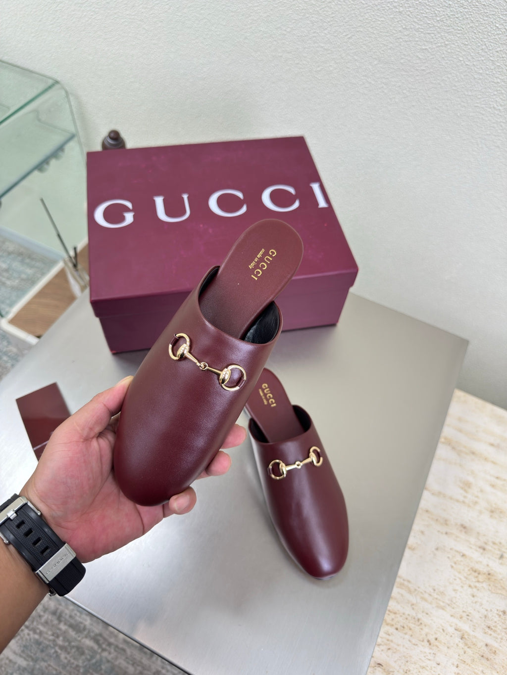 Burgundy leather Gucci mule held up, gold horsebit detail over a low flat sole