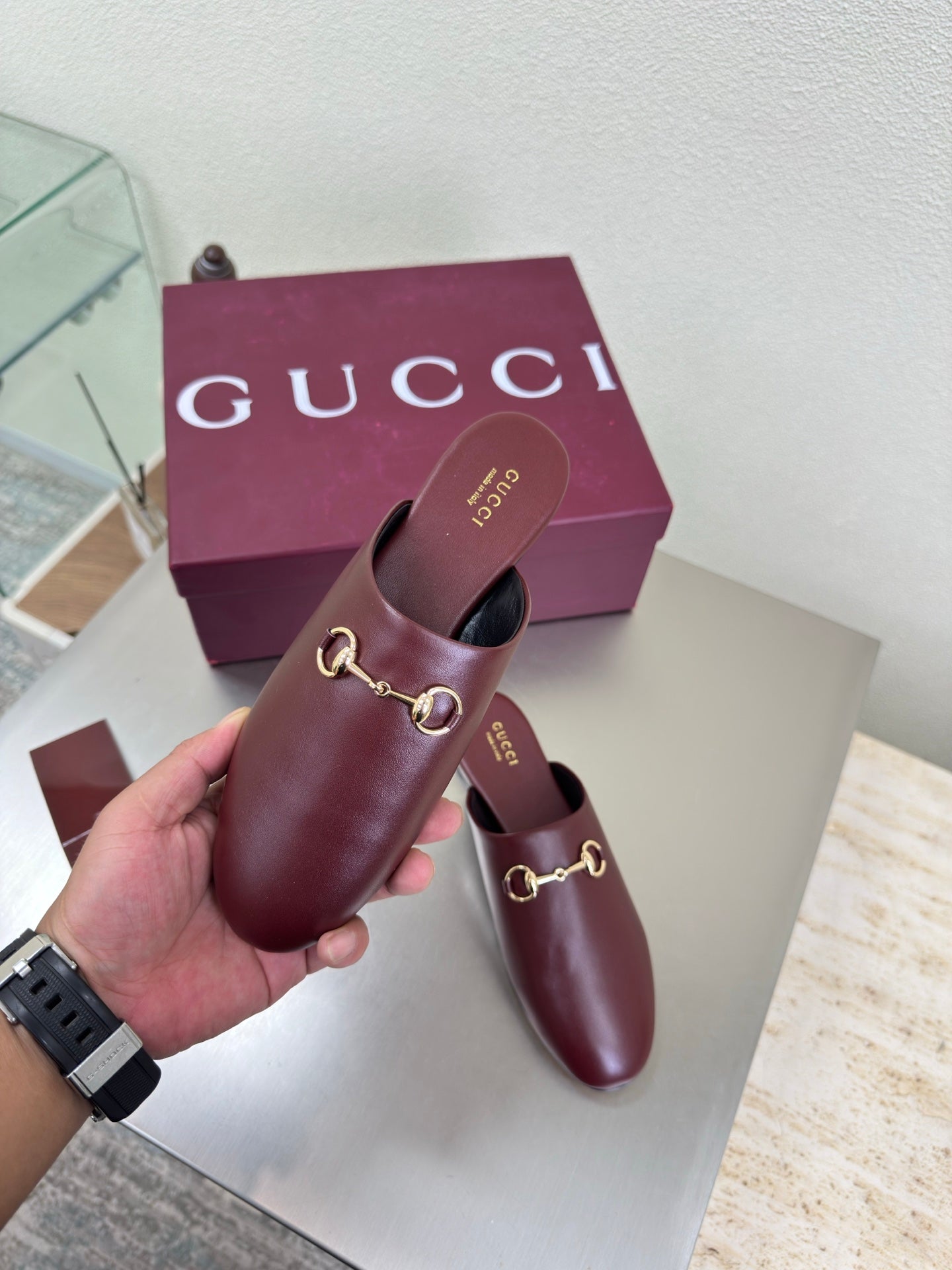 Burgundy leather Gucci mule held up, gold horsebit detail over a low flat sole