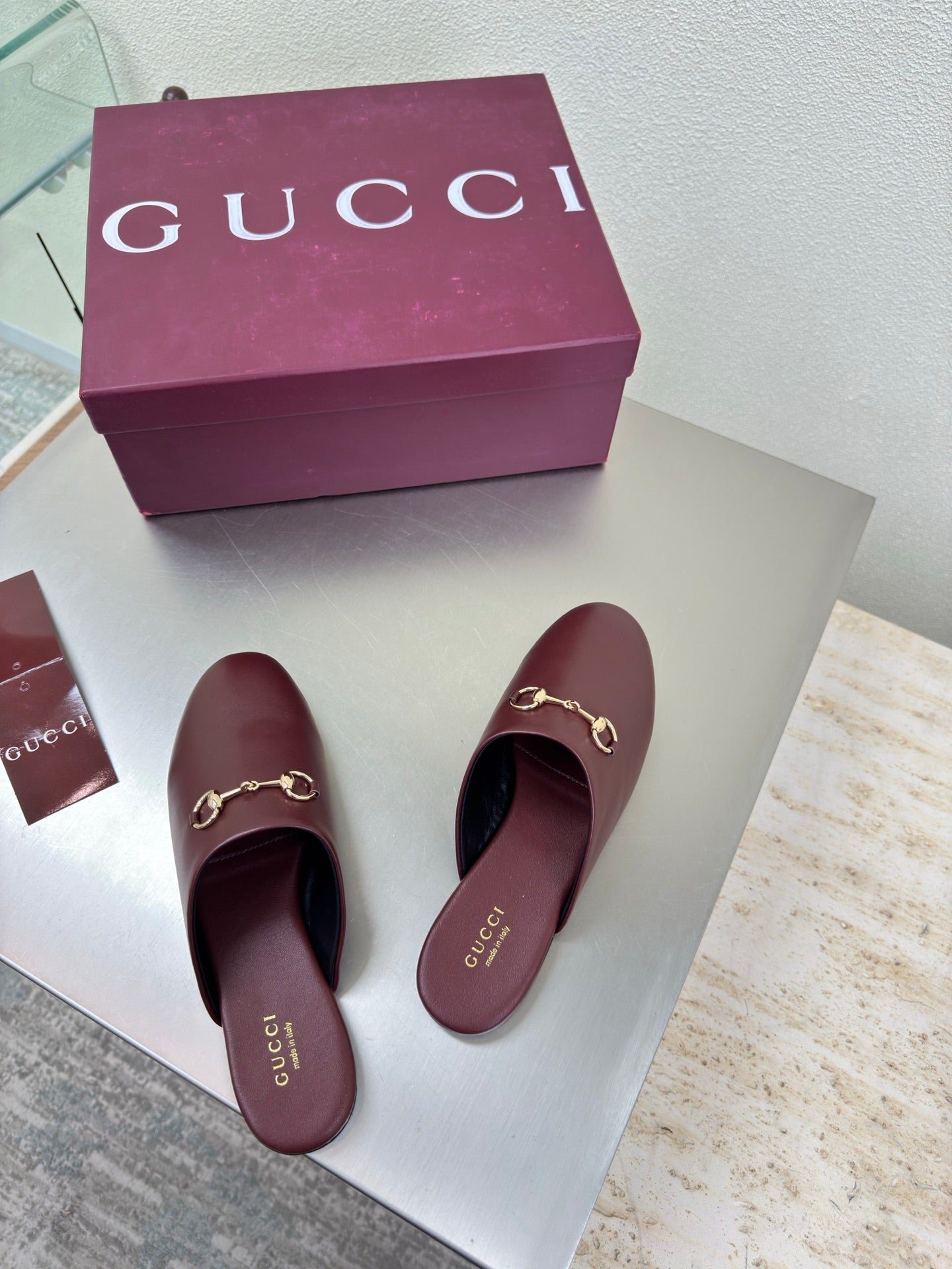 Two burgundy leather mules with gold horsebit hardware and rounded open toe shape