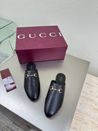 Gucci black leather mules with gold horsebit detail, purple box behind them