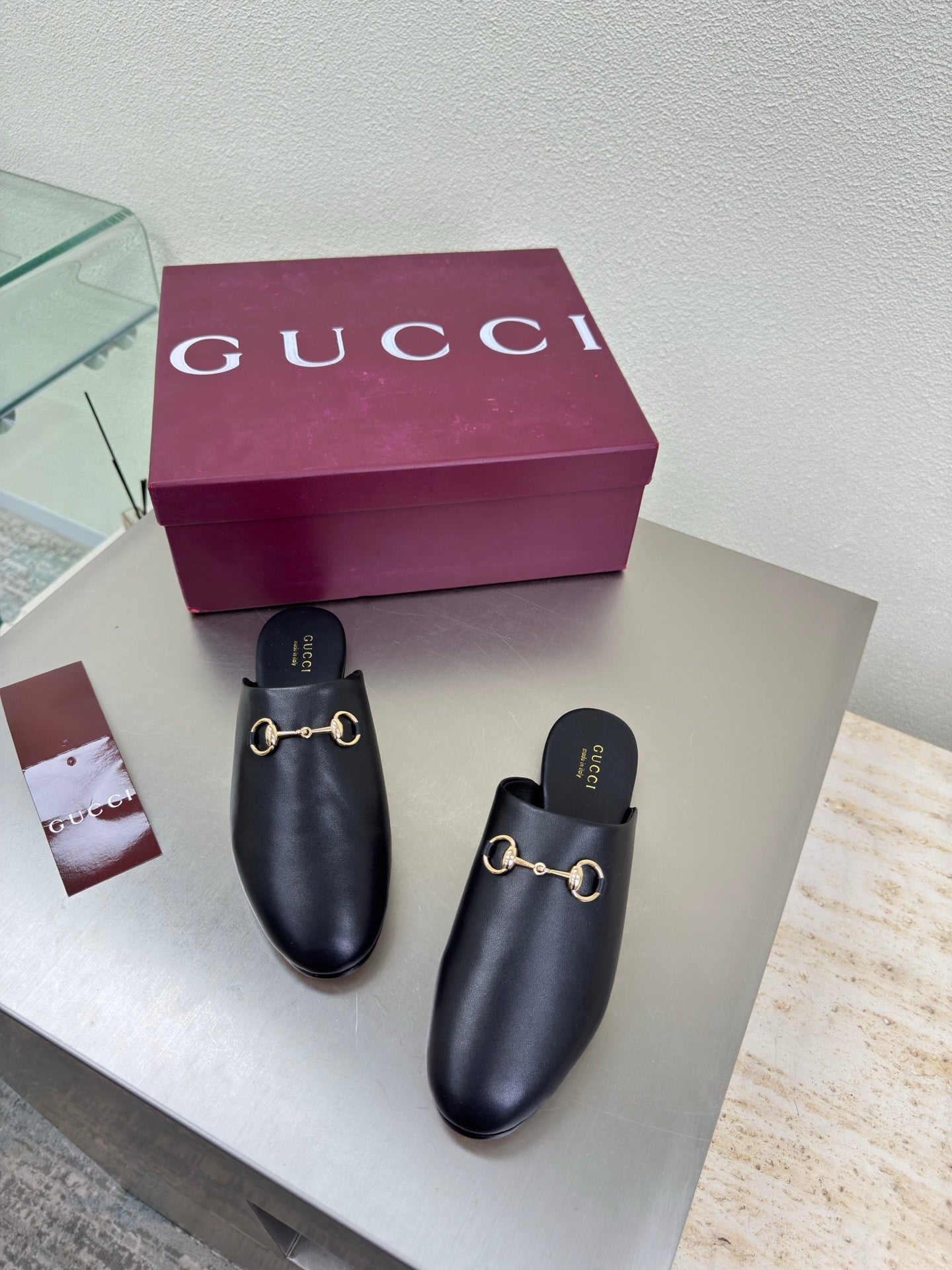 Gucci black leather mules with gold horsebit detail, purple box behind them