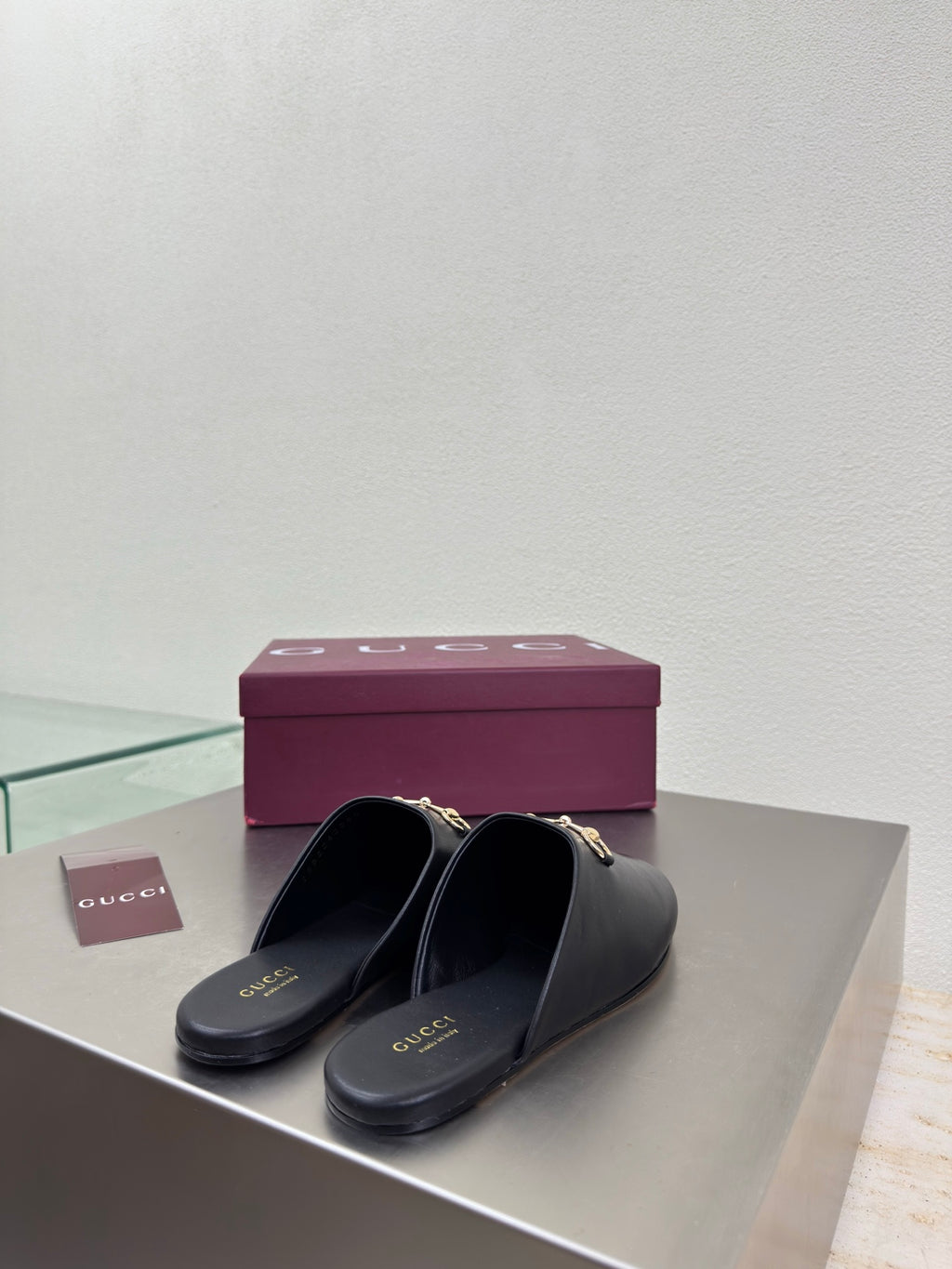 Two Gucci black leather mules with gold horsebit detail beside a purple logo box