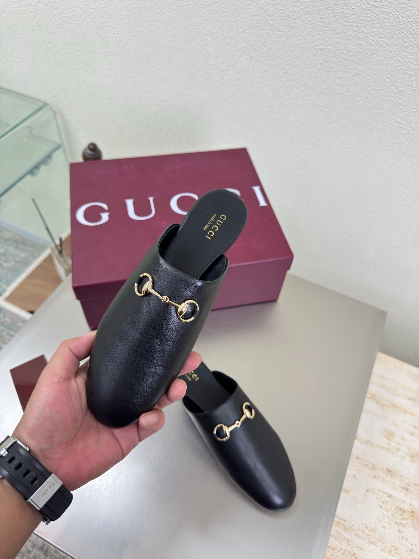 Hand holding a Gucci black leather mule with gold horsebit strap and rounded toe