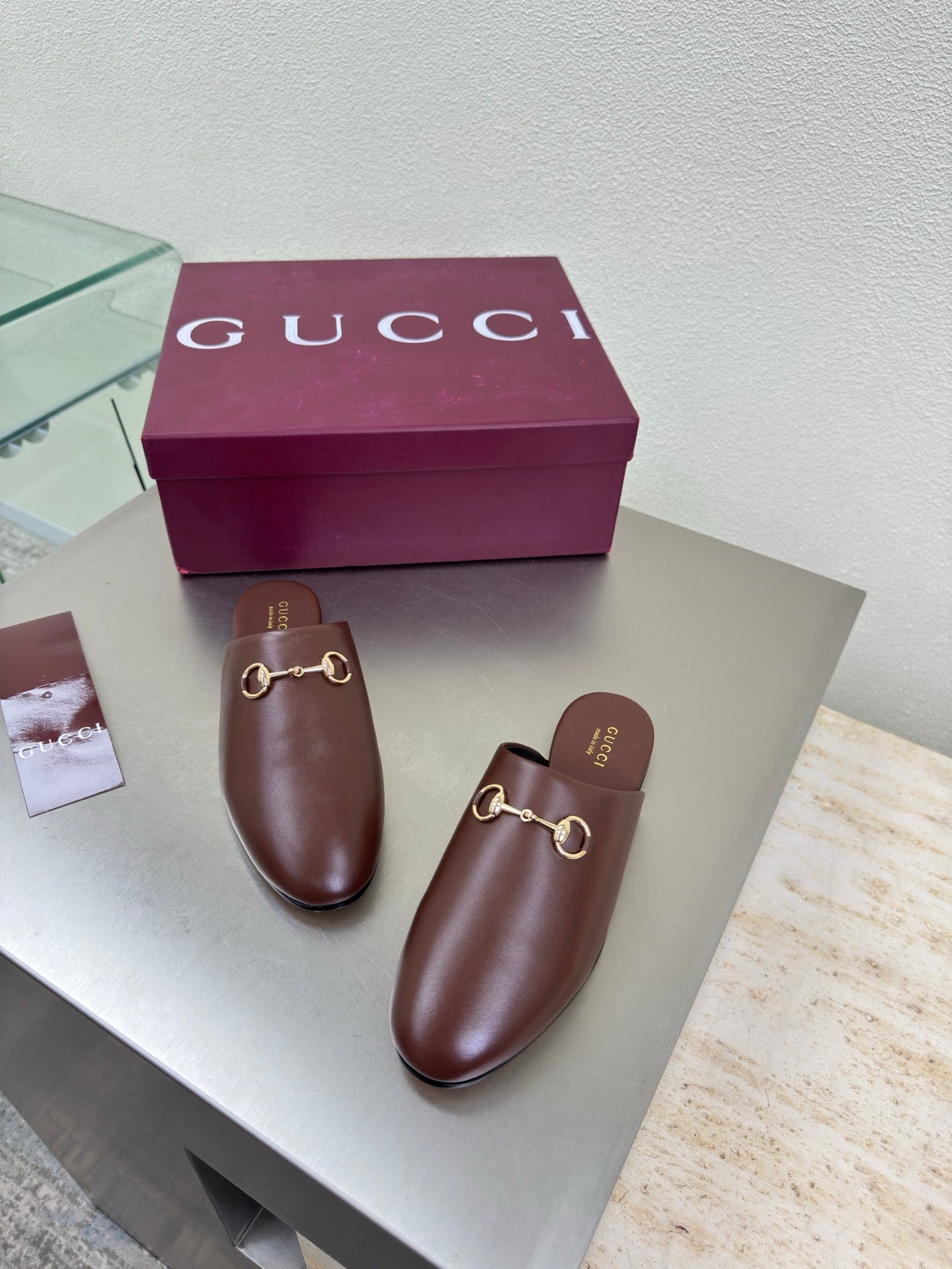 Two brown Gucci leather mules with gold horsebit front, on display with box