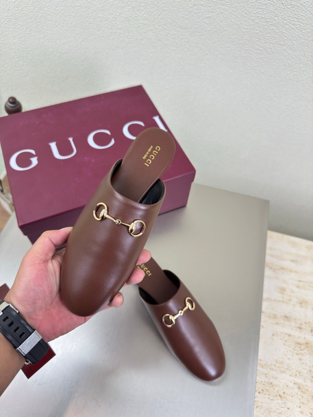 Gucci brown leather mule held in hand, gold horsebit strap on rounded toe