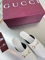 White mule shoes with gold horsebit hardware and black interior, side view pair