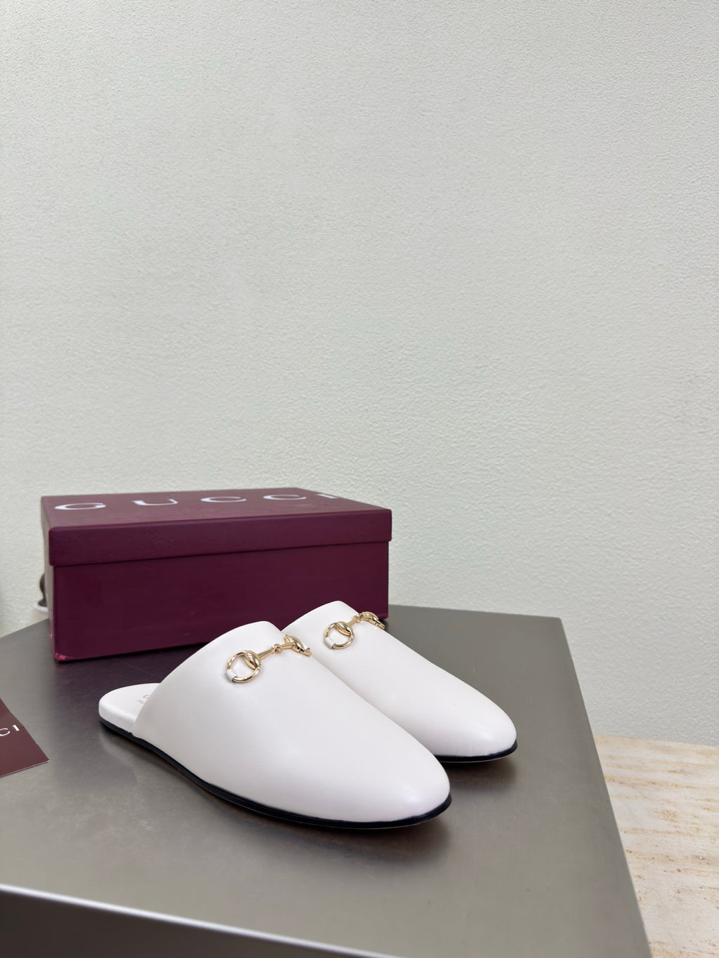 White mule shoe with gold horsebit hardware, side profile on display