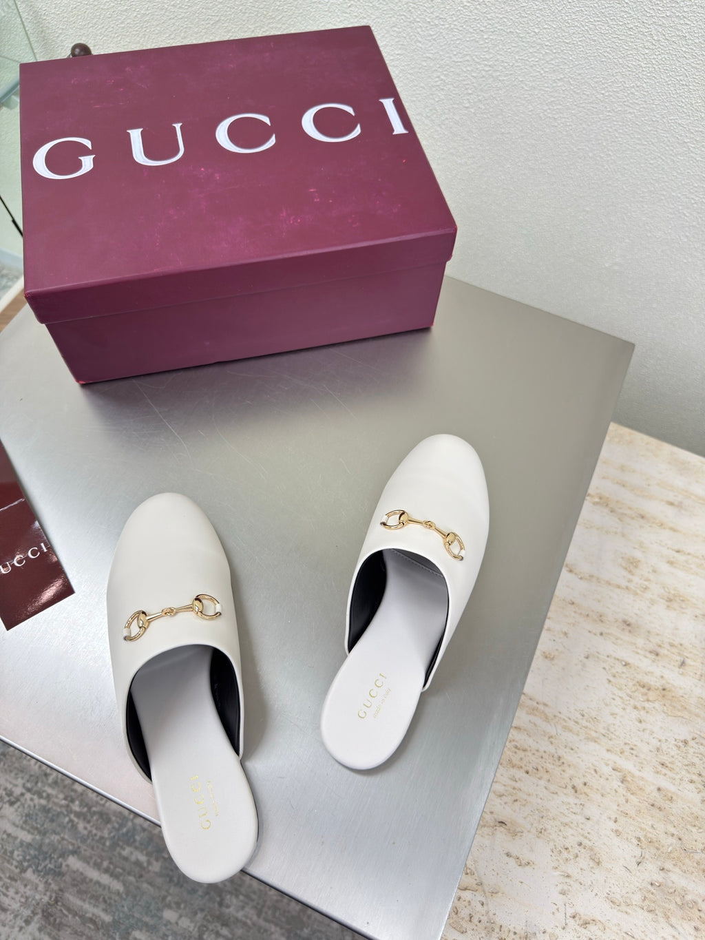 White mule shoes with gold horsebit detail, pair displayed on shoebox