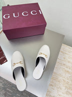 White mule shoes with gold horsebit detail, pair displayed on shoebox