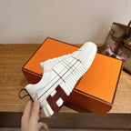 Hermes unisex white sneakers, lace-up with black grid stitching and thick rubber sole.