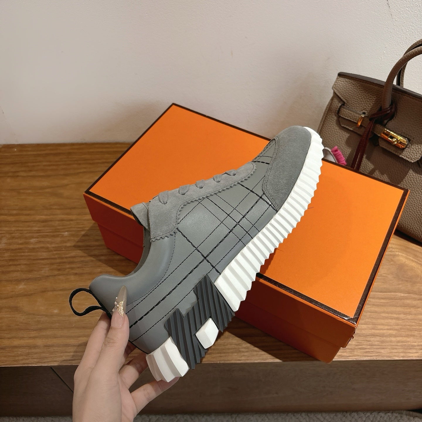 Gray lace-up sneaker with white ribbed sole and stitched grid panel on upper.
