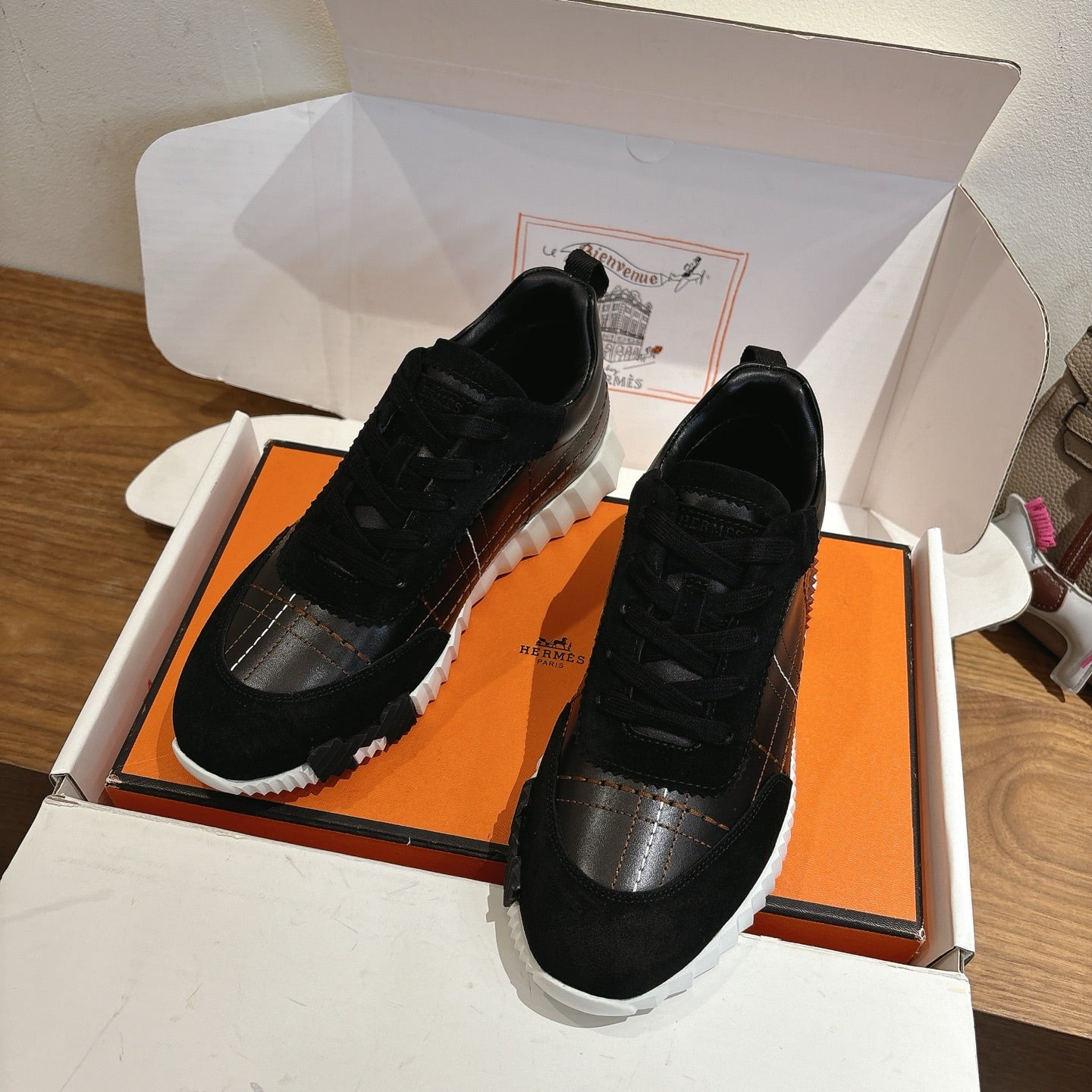 Black lace-up sneakers displayed on open box with white rubber sole