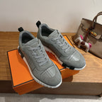 Two gray sneakers on an orange box, lace-up with grid stitching and white sole.