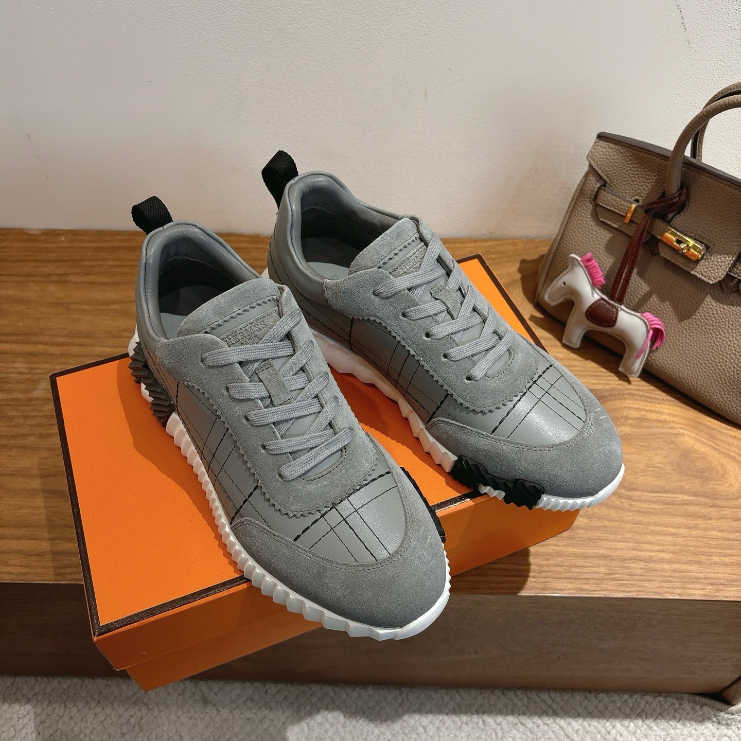 Two gray sneakers on an orange box, lace-up with grid stitching and white sole.