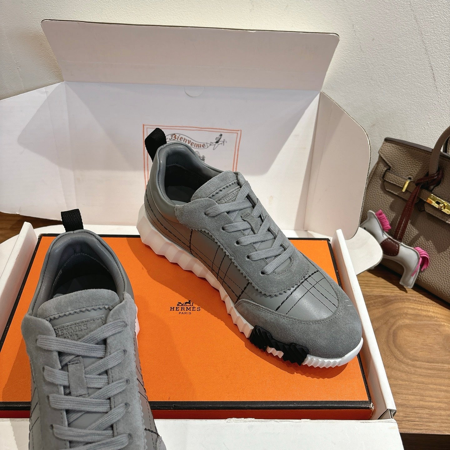 Gray sneakers on orange box insert, lace-up uppers with grid stitching and white sole.