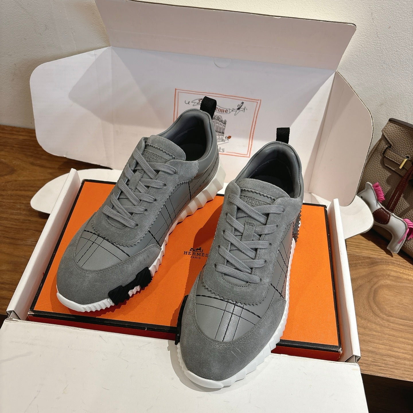 Gray lace-up sneakers in an open box, with black heel tabs and white rubber sole.