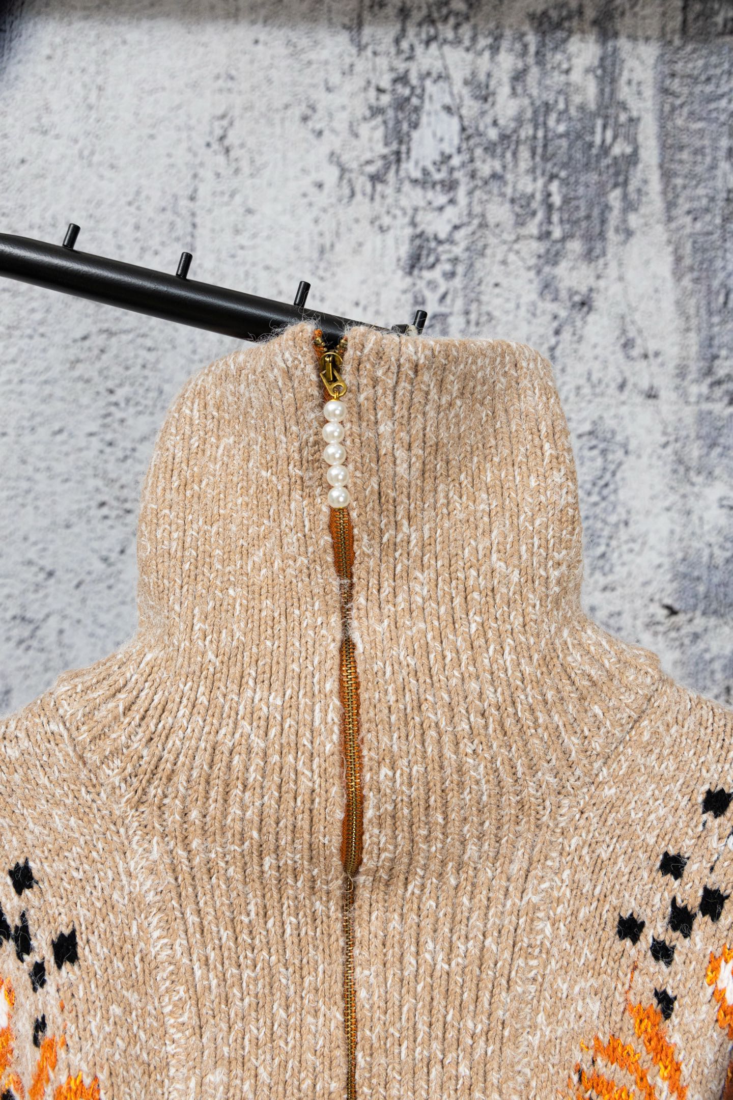 Beige knit turtleneck-style sweater with orange top and pearl-look bead necklace detail