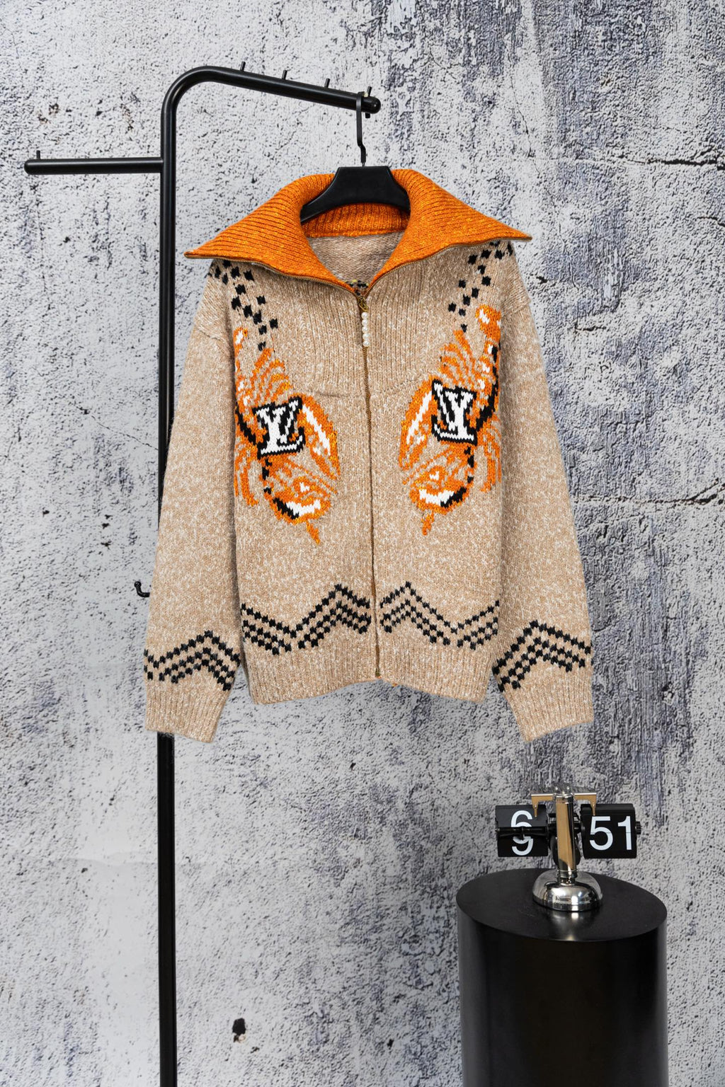 Beige knit zip-up sweater with orange hood, orange cuffs, and black geometric accents