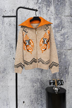 Beige knit zip-up sweater with orange hood, orange cuffs, and black geometric accents