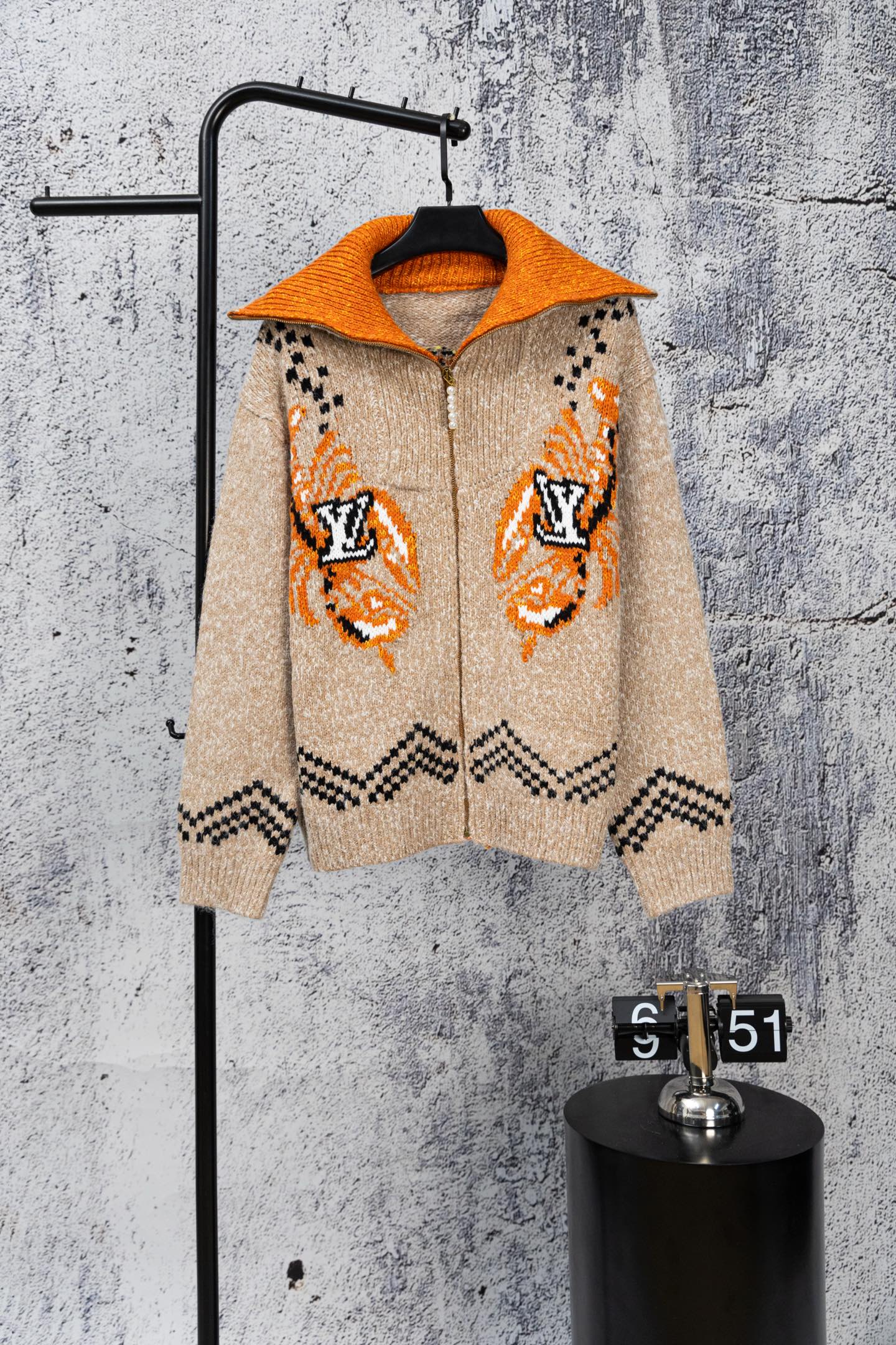Beige knit zip-up sweater with orange hood, orange cuffs, and black geometric accents