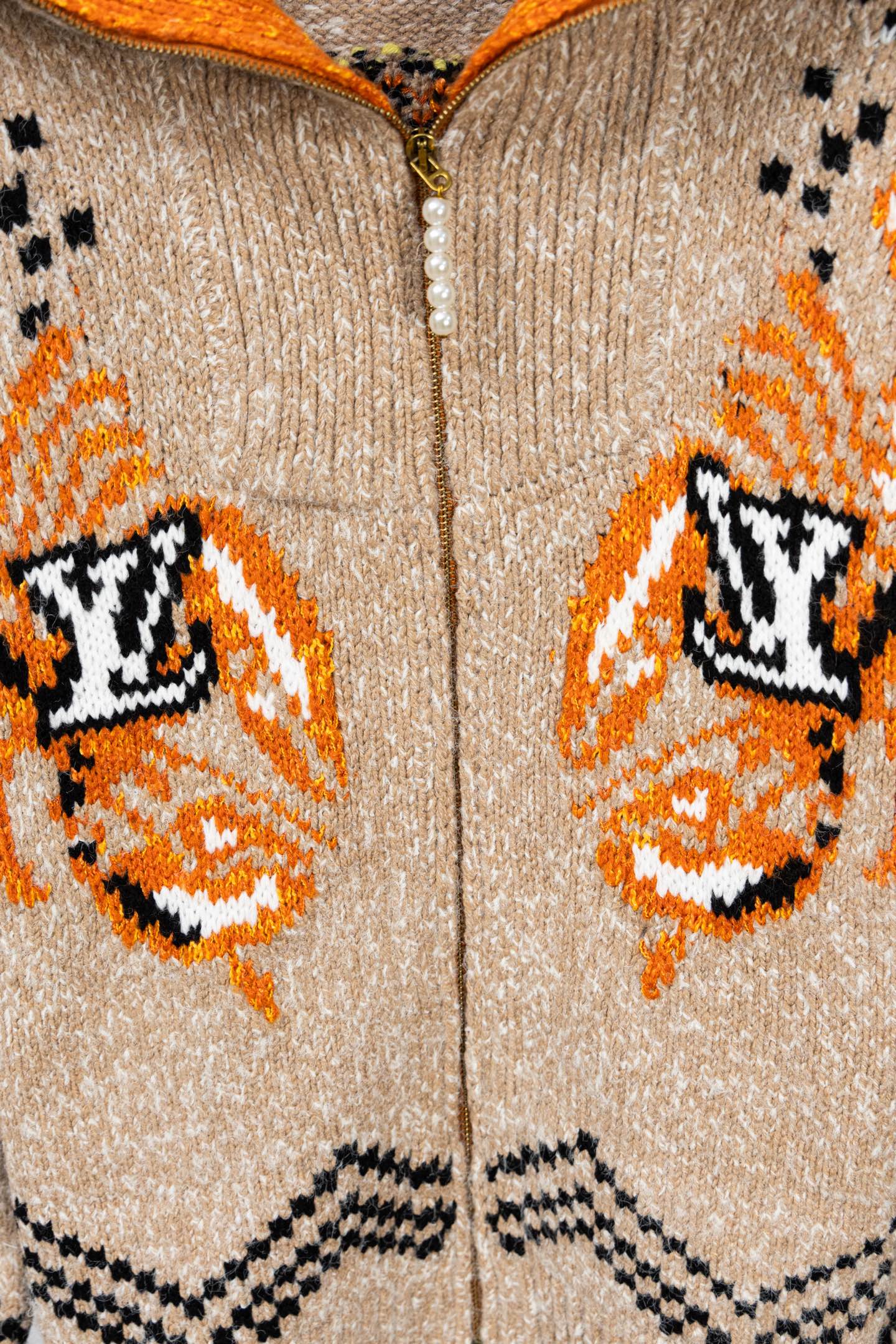 Beige knit zip-up sweater close-up with orange and black LV-style monogram patterns