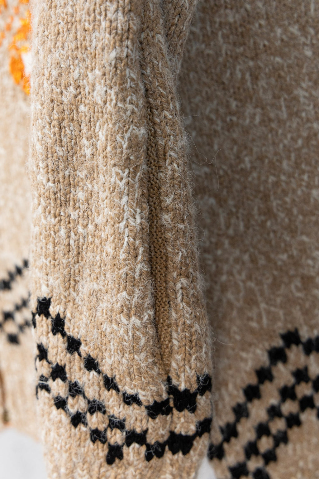 Beige knit sleeve with black zigzag trim and orange accent near cuff