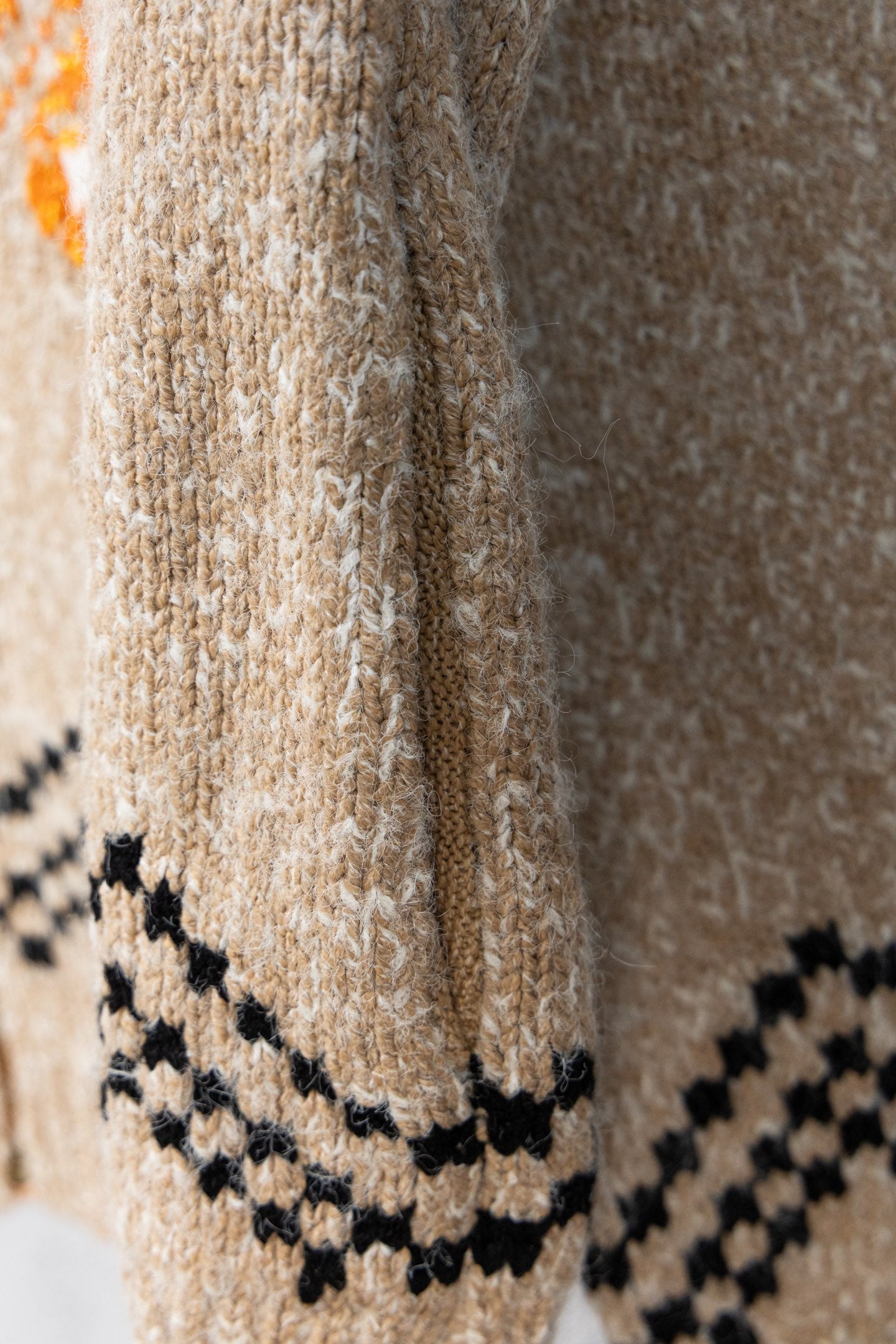 Beige knit sleeve with black zigzag trim and orange accent near cuff