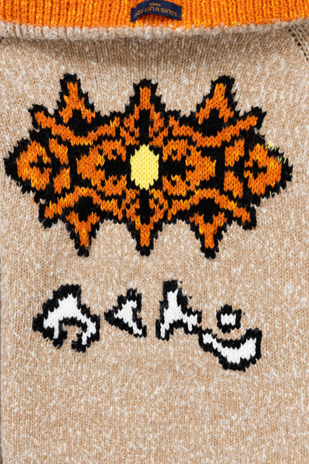 Beige knit zip-up sweater front with orange-and-black snowflake graphic and striped motifs