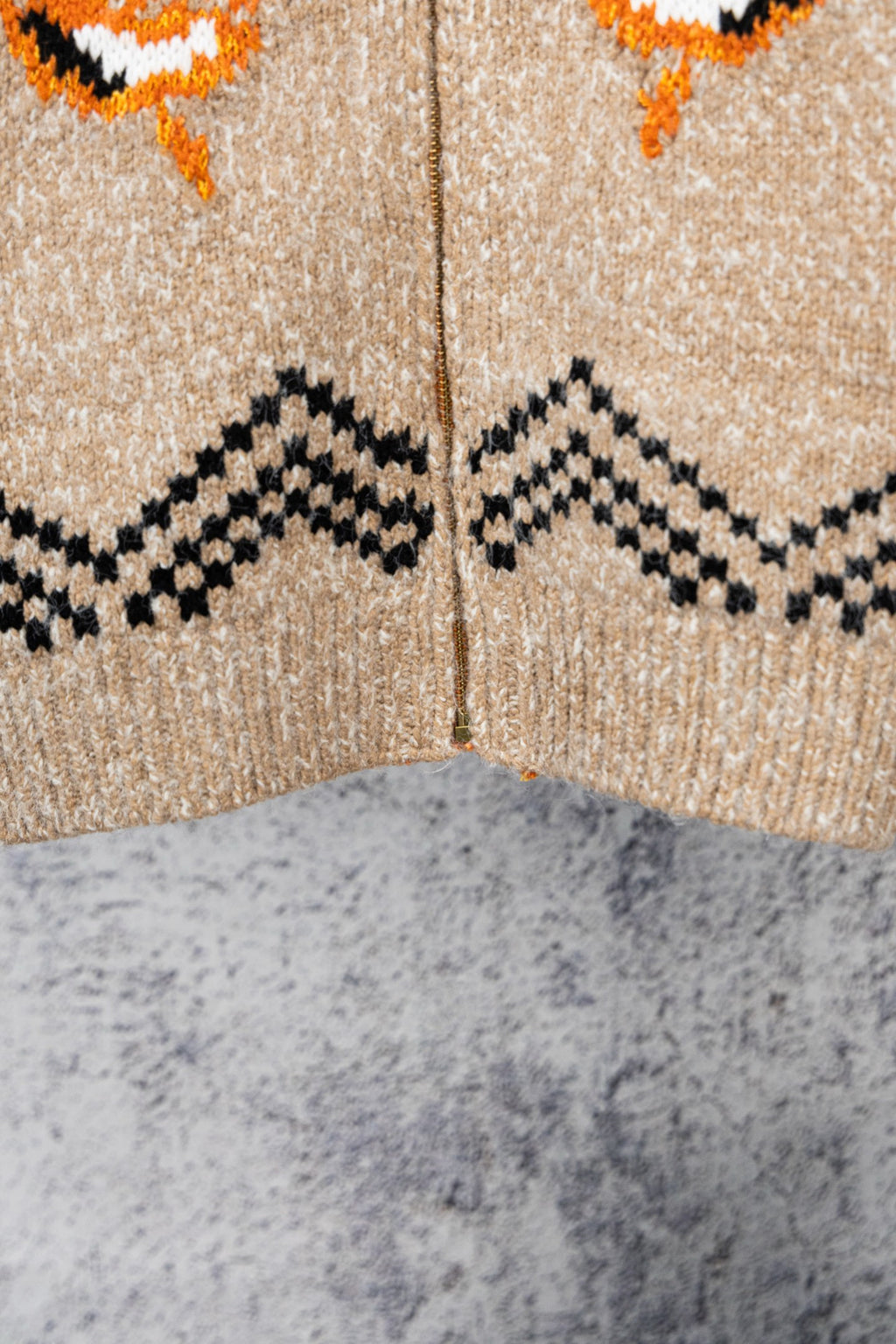 Beige knit zip-up sweater close-up with black zigzag and orange motifs across chest