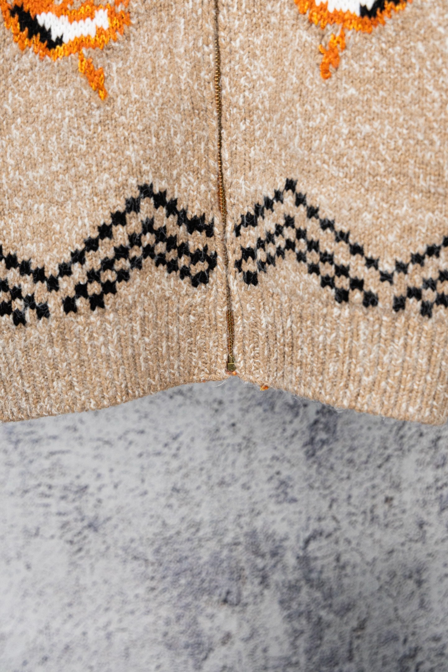 Beige knit zip-up sweater close-up with black zigzag and orange motifs across chest