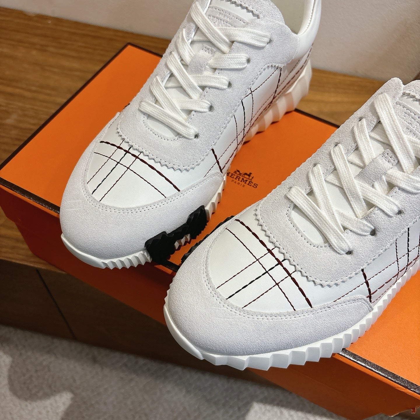 Hermes unisex white sneakers toe and side close-up, lace-up, black grid stitching, sole.