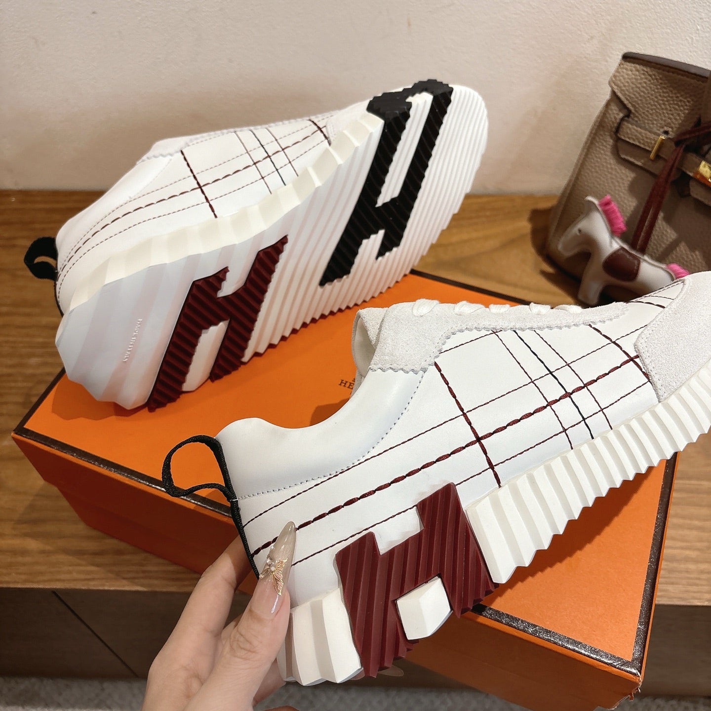 Hermes unisex white sneakers outsole and side view, chunky tread, black grid stitching.