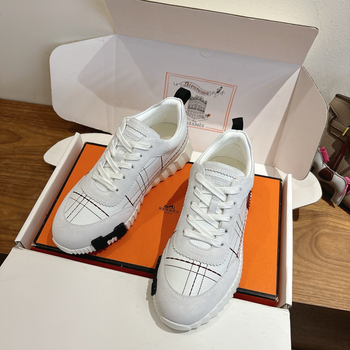Hermes unisex white sneakers in open box, lace-up, black grid stitching, rubber sole.