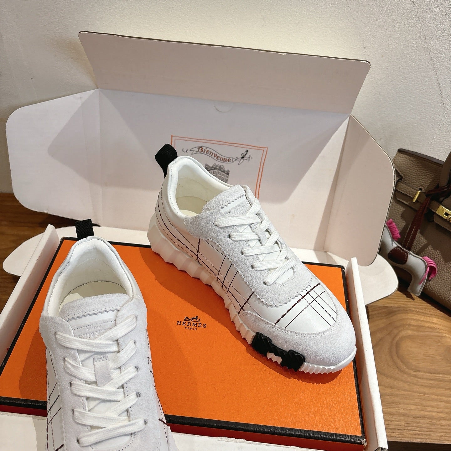 Hermes unisex white sneakers in box, lace-up with black grid stitching and rubber sole.