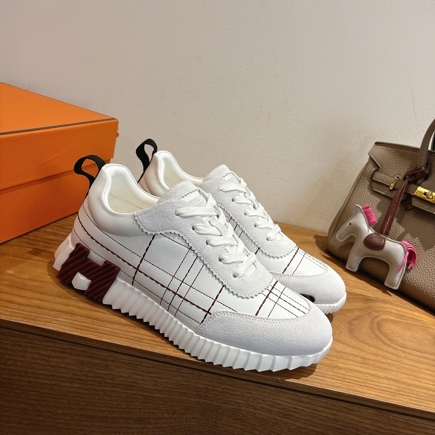 Hermes unisex white sneakers side view, lace-up, black grid panel stitching, rubber sole.
