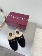 Black Gucci mules with beige shearling lining and GG pattern, on white display table.