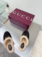 Black Gucci mules with beige shearling lining and GG pattern, on white display with maroon box.
