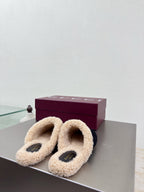 Pair of black Gucci mules with beige shearling lining and gold chain ornament, on shelf.
