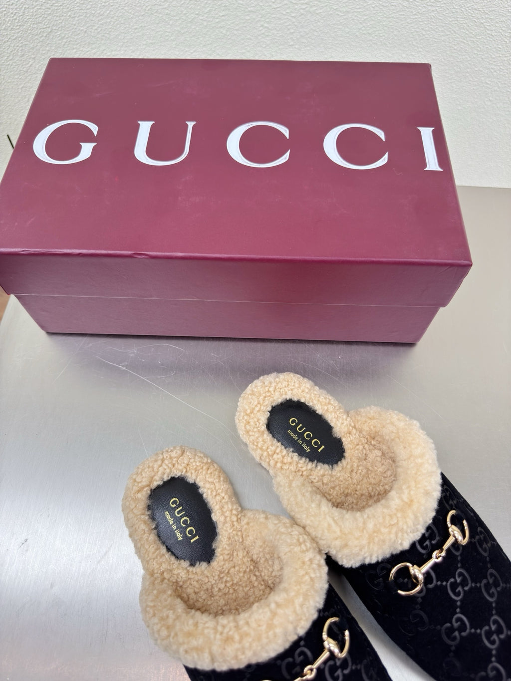 Black Gucci GG-pattern mules with beige shearling collar and gold-tone chain detail.