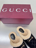 Black Gucci GG-pattern mules with beige shearling collar and gold-tone chain detail.