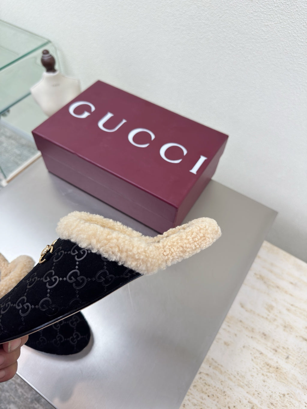Black Gucci mules with beige shearling trim and GG pattern, viewed from top-left.