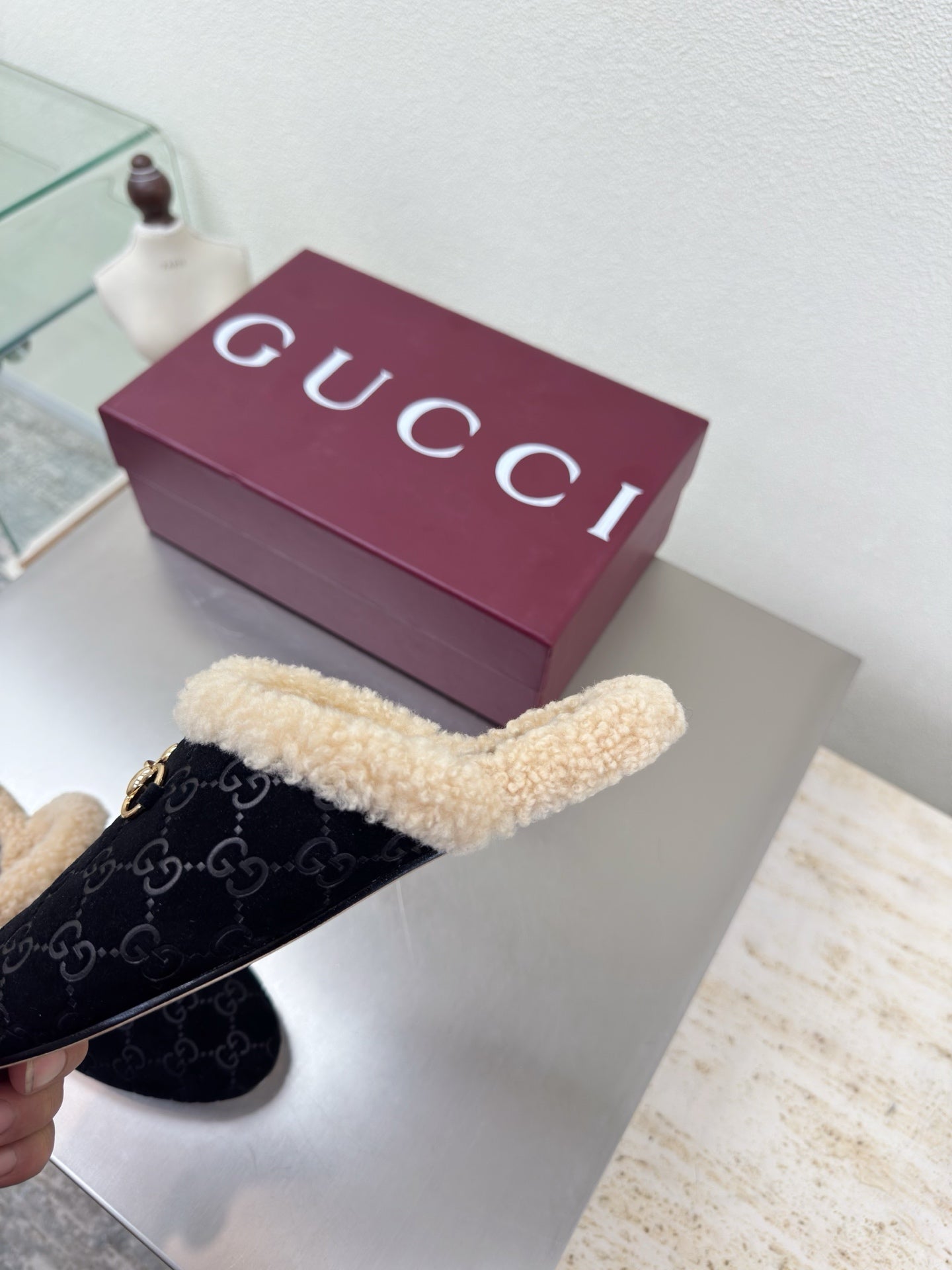 Black Gucci mules with beige shearling trim and GG pattern, viewed from top-left.