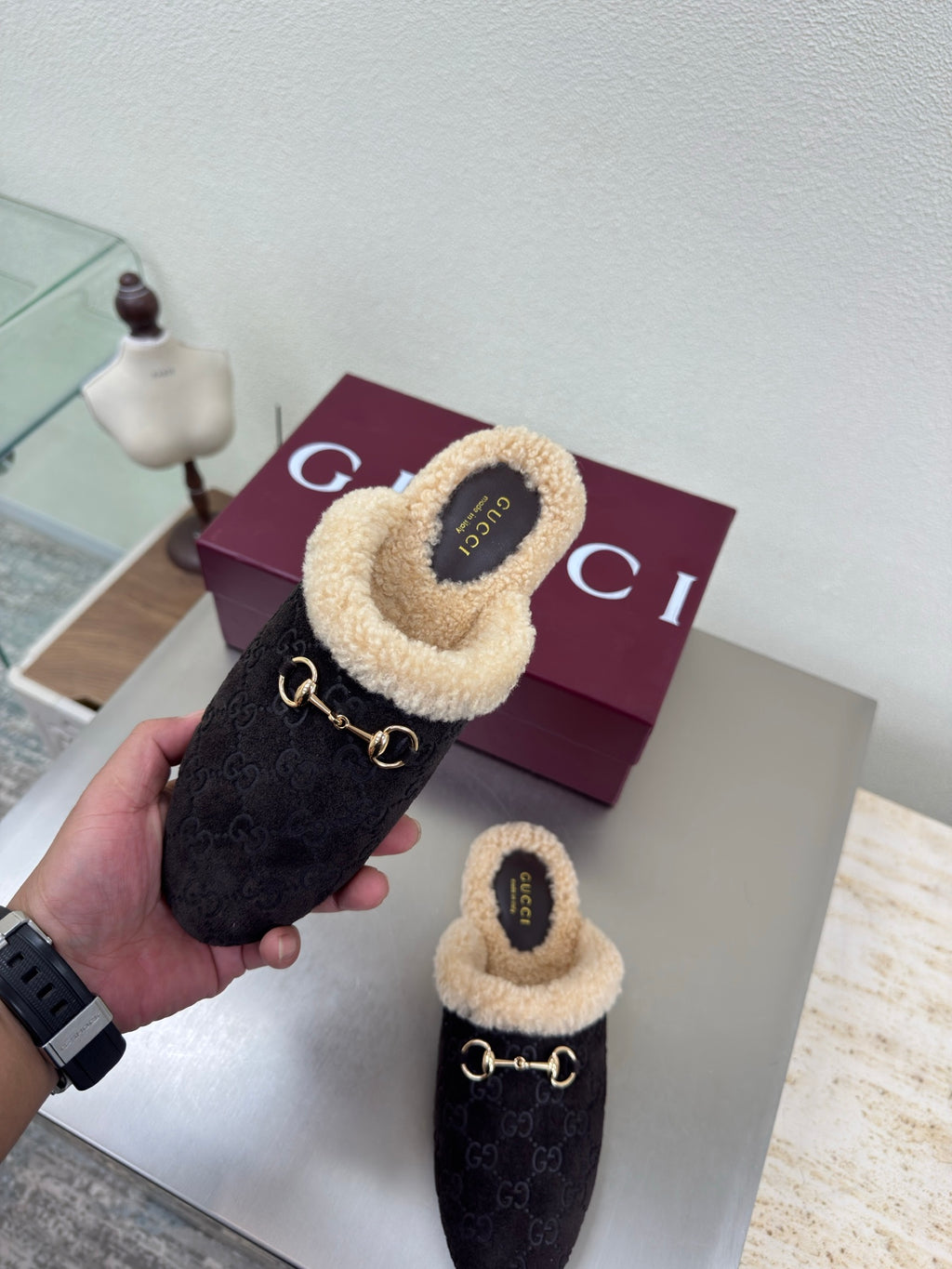Gucci women’s slipper shown in hand, dark monogram with tan shearling cuff and gold bit