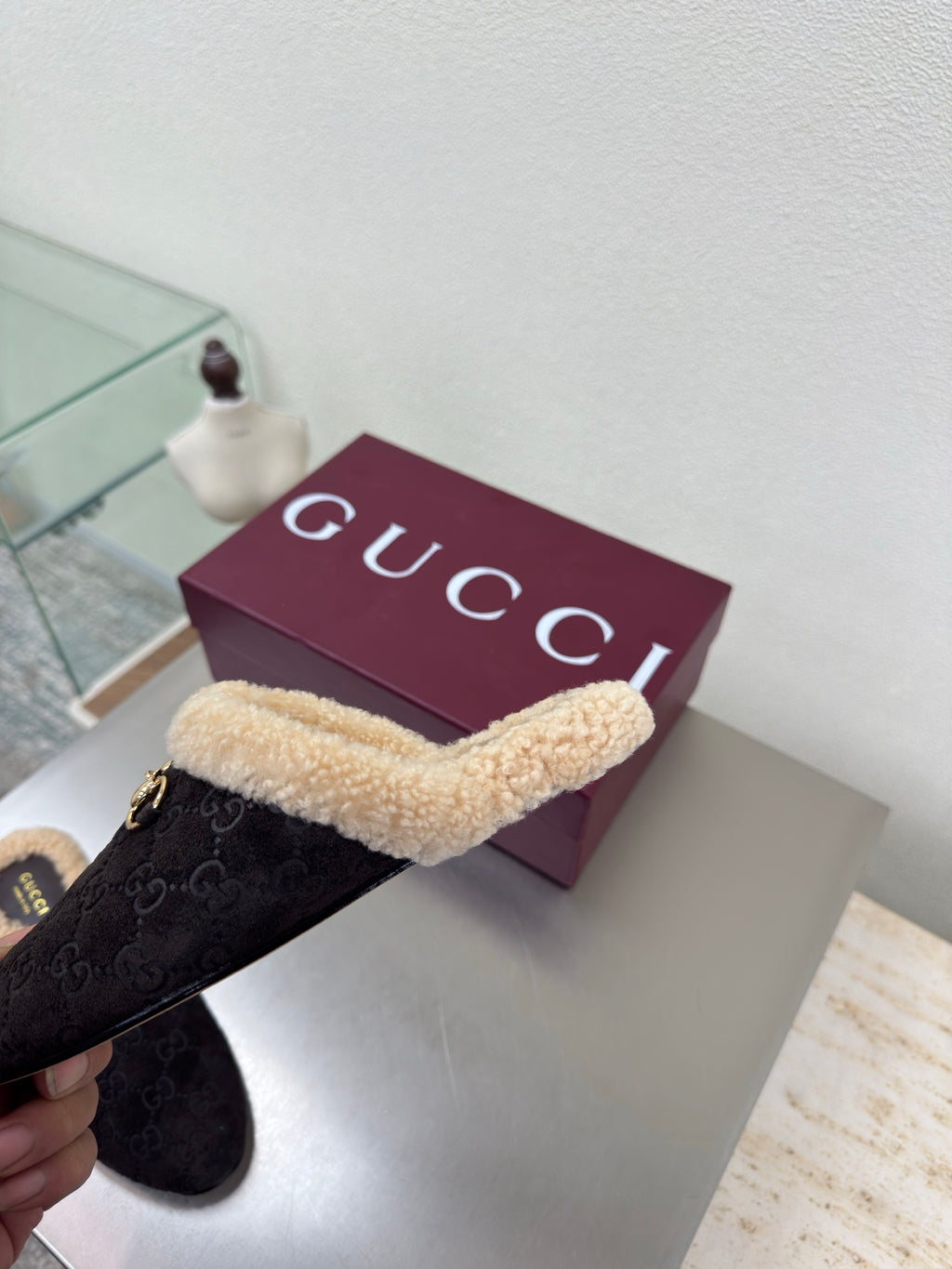 Gucci women’s slipper held sideways, dark monogram with tan shearling strap and gold bit