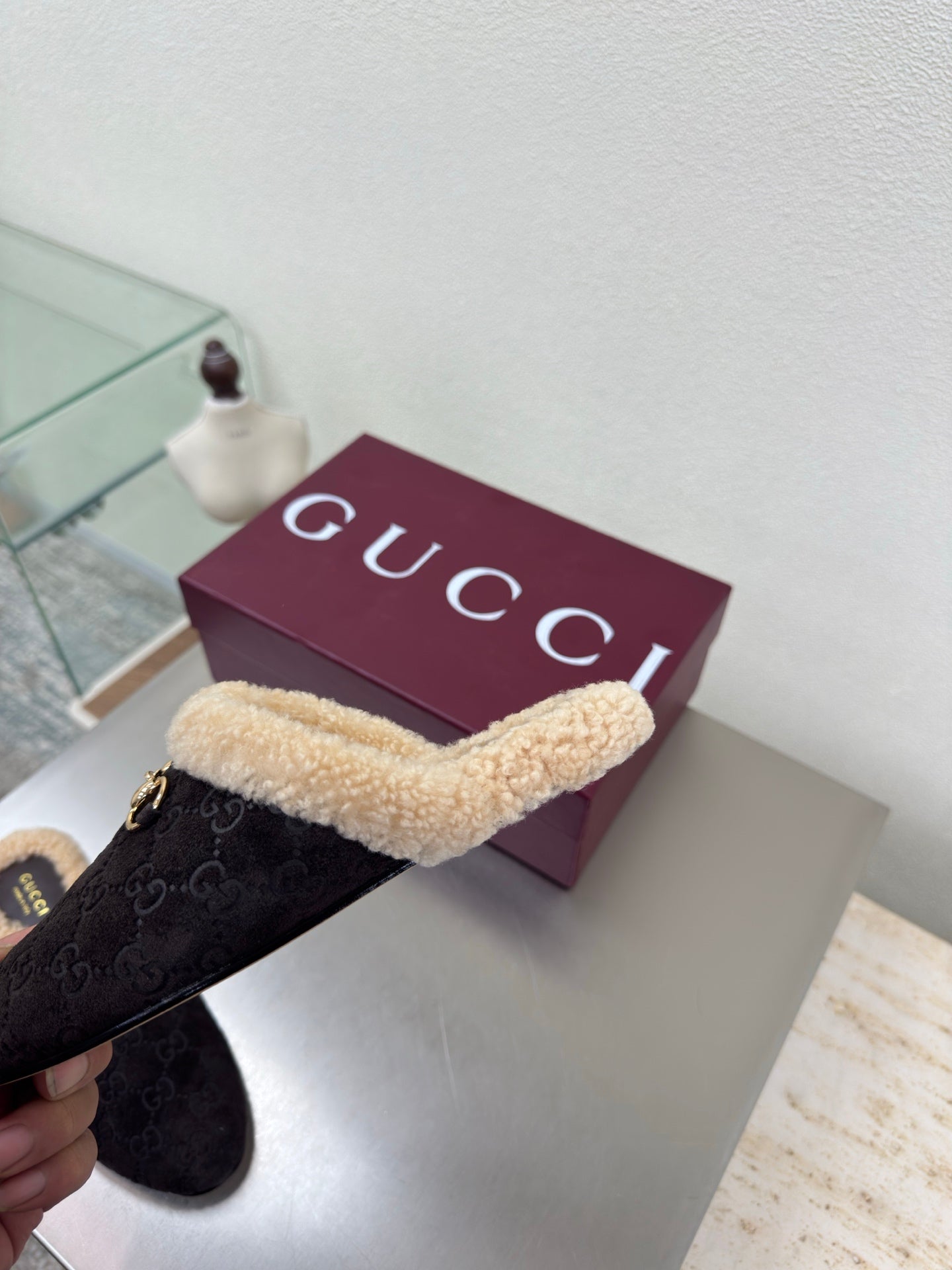 Gucci women’s slipper held sideways, dark monogram with tan shearling strap and gold bit