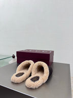 Gucci women’s slippers with dark uppers, tan shearling straps, and gold bit accents